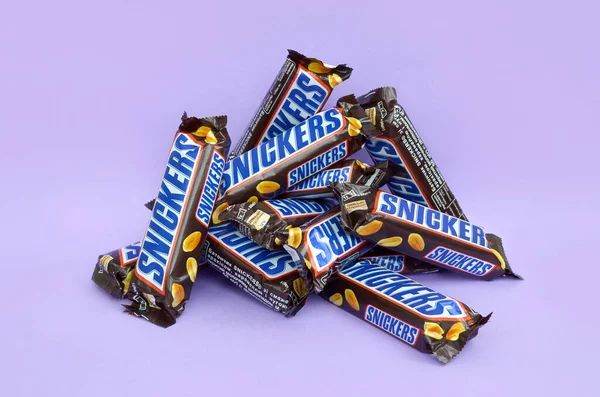 Muitas barras de chocolate Snickers encontra-se em papel lilás pastel. Barras Snickers são produzidas pela Mars Incorporated. Snickers foi criado por Franklin Clarence Mars em 1930 — Fotografia de Stock