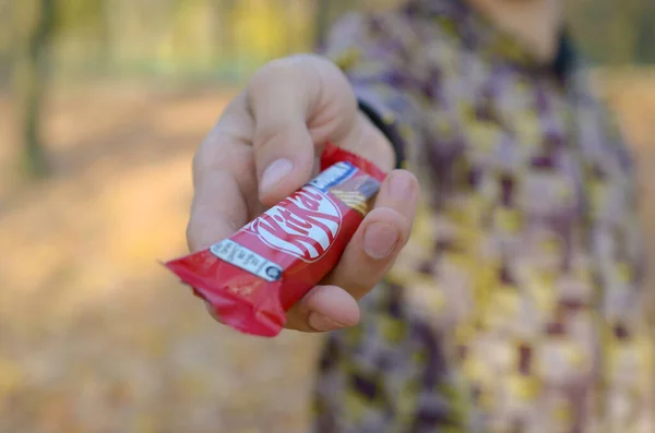 KHARKOV, UCRÂNIA - OUTUBRO 21, 2019: Jovem passa por uma barra de chocolate Kit kat em um parque de outono. A manifestação da bondade, tratando com doces — Fotografia de Stock