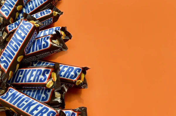 Veel Snickers chocoladerepen liggen op pasteloranje papier. Snickers bars worden geproduceerd door Mars Incorporated. Snickers is gemaakt door Franklin Clarence Mars in 1930. — Stockfoto