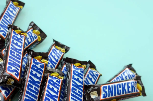 Many Snickers chocolate bars lies on pastel blue paper. Snickers bars are produced by Mars Incorporated. Snickers was created by Franklin Clarence Mars in 1930