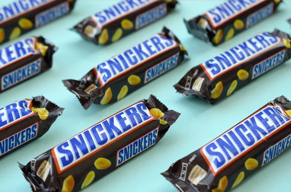 Many Snickers chocolate bars lies on pastel blue paper. Snickers bars are produced by Mars Incorporated. Snickers was created by Franklin Clarence Mars in 1930 — Stock fotografie