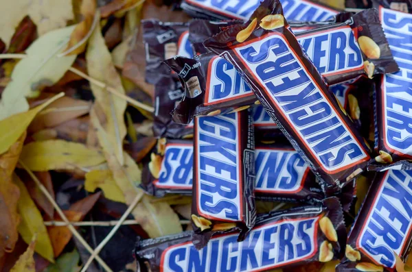 Snickers barras de chocolate em marrom embrulho mentiras sobre folhas de outono fundo — Fotografia de Stock
