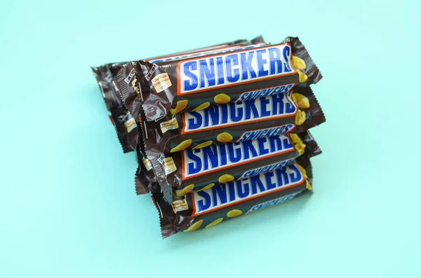 Many Snickers chocolate bars lies on pastel blue paper. Snickers bars are produced by Mars Incorporated. Snickers was created by Franklin Clarence Mars in 1930