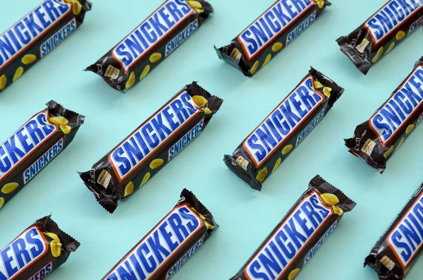Many Snickers chocolate bars lies on pastel blue paper. Snickers bars are produced by Mars Incorporated. Snickers was created by Franklin Clarence Mars in 1930
