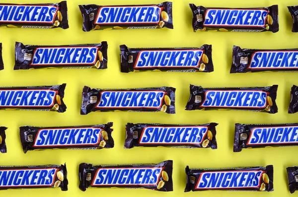 Många Snickers chokladkakor ligger på pastellgult papper. Snickers barer tillverkas av Mars Incorporated. Snickers skapades av Franklin Clarence Mars 1930 — Stockfoto