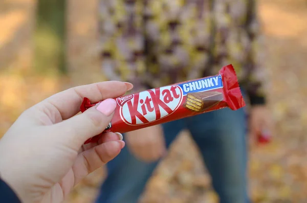 KHARKOV, UCRANIA - 21 DE OCTUBRE DE 2019: Mano masculina pasa a la chica una barra de chocolate Kit kat en un parque de otoño. La manifestación de la bondad, el tratamiento con dulces — Foto de Stock