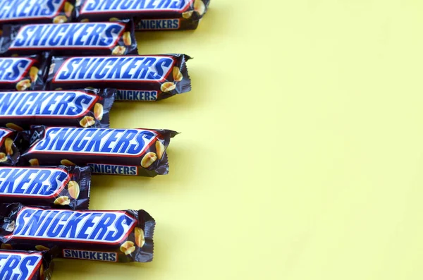 Muitas barras de chocolate Snickers encontra-se em papel amarelo pastel. Barras Snickers são produzidas pela Mars Incorporated. Snickers foi criado por Franklin Clarence Mars em 1930 — Fotografia de Stock