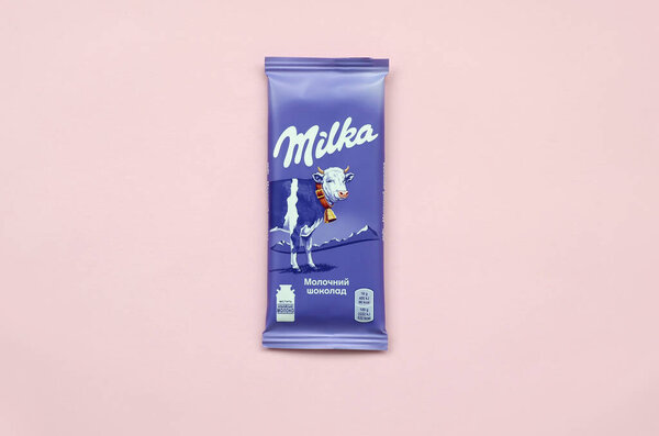 Milka chocolate tablet in classic violet wrapping on pastel pink background. Milka is brand of chocolate confection originated in Switzerland in 1901