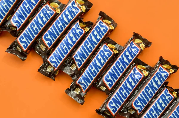 Veel Snickers chocoladerepen liggen op pasteloranje papier. Snickers bars worden geproduceerd door Mars Incorporated. Snickers is gemaakt door Franklin Clarence Mars in 1930. — Stockfoto