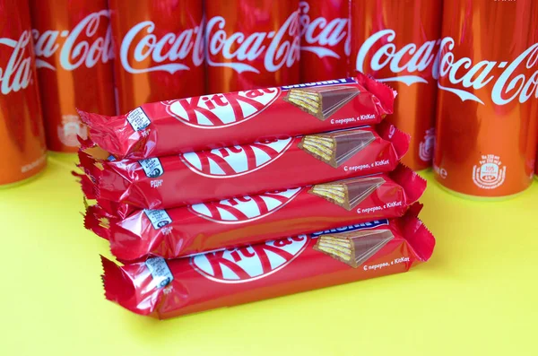 Kit Kat barras de chocolate en envoltura roja se encuentra sobre fondo amarillo brillante con latas de Coca Cola de cerca. Famoso producto de bebida y chocolate —  Fotos de Stock