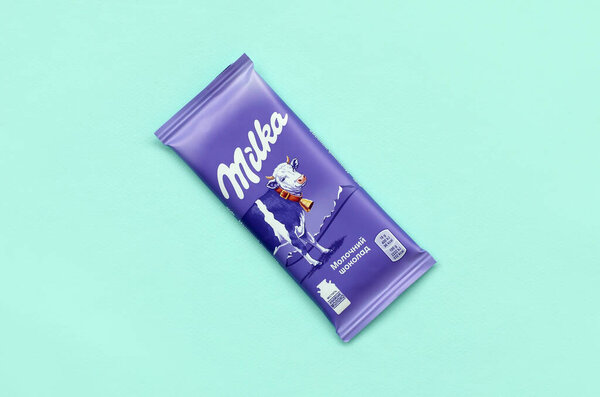 Milka chocolate tablet in classic violet wrapping on pastel blue background. Milka is brand of chocolate confection originated in Switzerland in 1901
