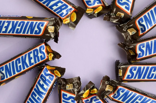 Muitas barras de chocolate Snickers encontra-se em papel lilás pastel. Barras Snickers são produzidas pela Mars Incorporated. Snickers foi criado por Franklin Clarence Mars em 1930 — Fotografia de Stock