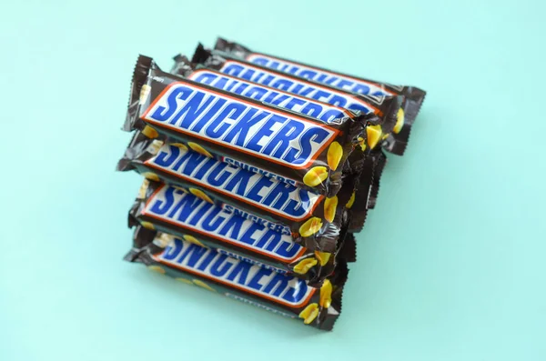 Muchas barras de chocolate Snickers se encuentra en papel azul pastel. Las barras Snickers son producidas por Mars Incorporated. Snickers fue creado por Franklin Clarence Mars en 1930 — Foto de Stock