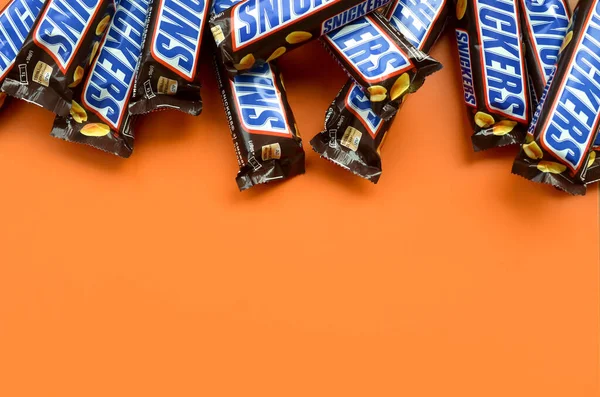 Many Snickers chocolate bars lies on pastel orange paper. Snickers bars are produced by Mars Incorporated. Snickers was created by Franklin Clarence Mars in 1930 — Stock Photo, Image