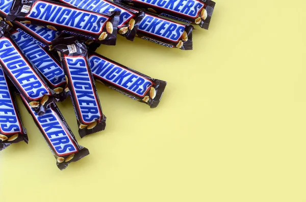 Muitas barras de chocolate Snickers encontra-se em papel amarelo pastel. Barras Snickers são produzidas pela Mars Incorporated. Snickers foi criado por Franklin Clarence Mars em 1930 — Fotografia de Stock