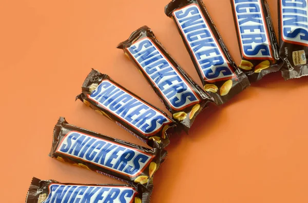 Muitas barras de chocolate Snickers encontra-se em papel laranja pastel. Barras Snickers são produzidas pela Mars Incorporated. Snickers foi criado por Franklin Clarence Mars em 1930 — Fotografia de Stock