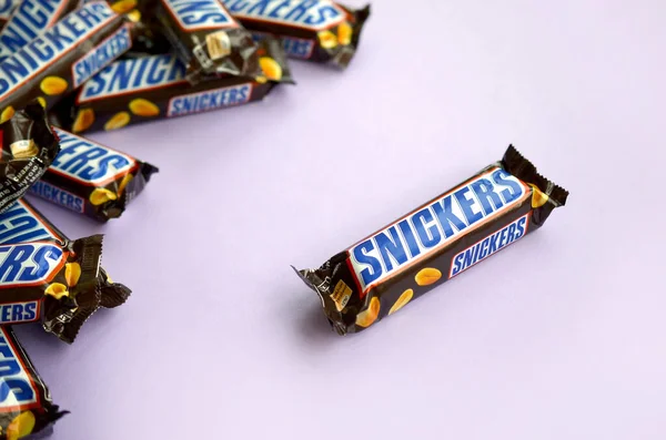 Veel Snickers chocoladerepen liggen op pastellila papier. Snickers bars worden geproduceerd door Mars Incorporated. Snickers is gemaakt door Franklin Clarence Mars in 1930. — Stockfoto