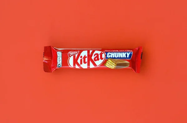 Kit Kat chocolate bar in red wrapping lies on bright red background. Kit kat created by Rowntree's of York in United Kingdom and is now produced globally by Nestle — 图库照片