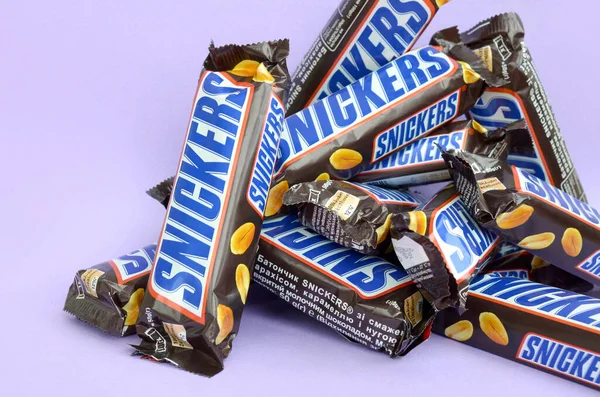 Många Snickers chokladkakor ligger på pastellpapper. Snickers barer tillverkas av Mars Incorporated. Snickers skapades av Franklin Clarence Mars 1930 — Stockfoto