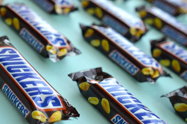 Muitas barras de chocolate Snickers encontra-se no papel azul pastel. Barras Snickers são produzidas pela Mars Incorporated. Snickers foi criado por Franklin Clarence Mars em 1930 — Fotografia de Stock