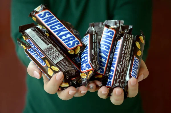 Kharkov, Oekraïne - 8 oktober 2019: Een jong Kaukasisch brunette meisje toont vele Snickers chocoladerepen in de donkere kamer. Snickers chocolade gemaakt door Mars — Stockfoto