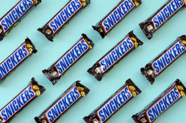 Muchas barras de chocolate Snickers se encuentra en papel azul pastel. Las barras Snickers son producidas por Mars Incorporated. Snickers fue creado por Franklin Clarence Mars en 1930 — Foto de Stock