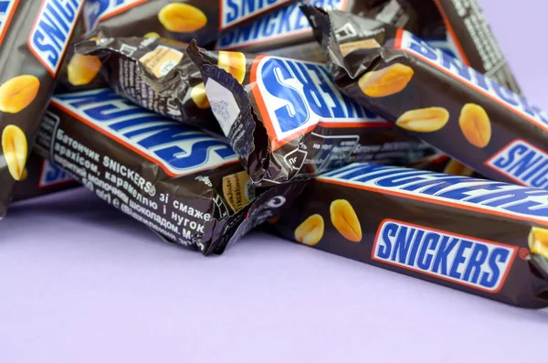 Veel Snickers chocoladerepen liggen op pastellila papier. Snickers bars worden geproduceerd door Mars Incorporated. Snickers is gemaakt door Franklin Clarence Mars in 1930. — Stockfoto