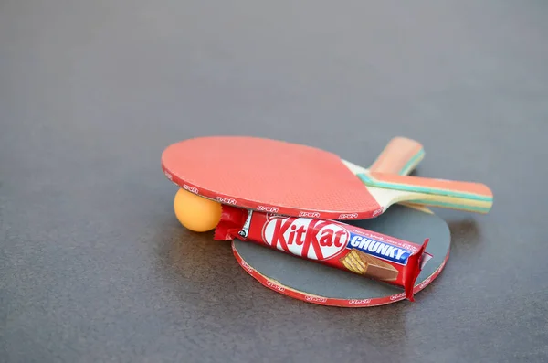 KHARKOV, UKRAINE - OCTOBER 17, 2019: Kit kat chocolate bar in red wrapping next to ping pong rackets and balls on table in a outdoor sport yard — Stock Photo, Image