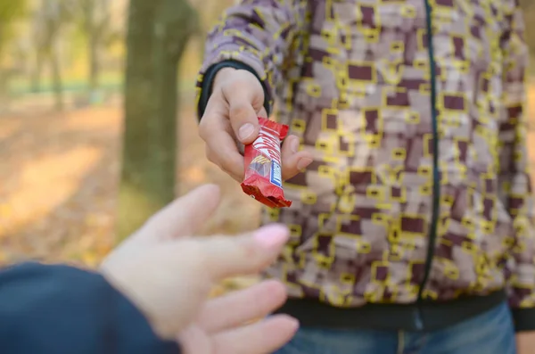 KHARKOV, UCRANIA - 21 DE OCTUBRE DE 2019: Mano masculina pasa a la chica una barra de chocolate Kit kat en un parque de otoño. La manifestación de la bondad, el tratamiento con dulces — Foto de Stock
