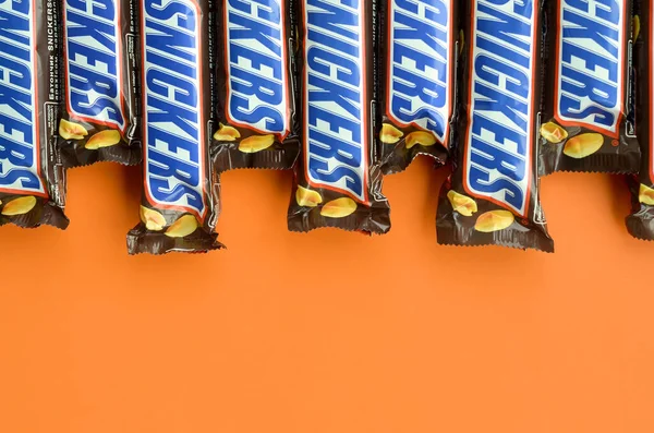 Muitas barras de chocolate Snickers encontra-se em papel laranja pastel. Barras Snickers são produzidas pela Mars Incorporated. Snickers foi criado por Franklin Clarence Mars em 1930 — Fotografia de Stock