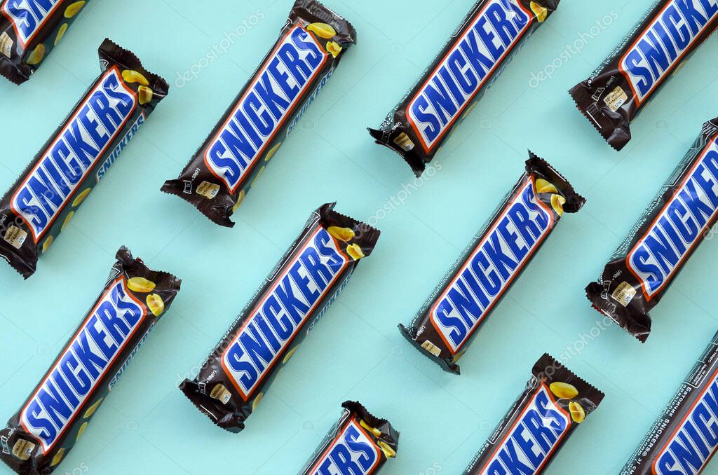 KHARKOV, UKRAINE - OCTOBER 2, 2019: Many Snickers chocolate bars lies on pastel blue paper. Snickers bars are produced by Mars Incorporated. Snickers was created by Franklin Clarence Mars in 1930