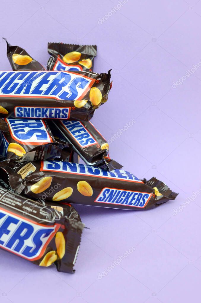 KHARKOV, UKRAINE - OCTOBER 2, 2019: Many Snickers chocolate bars lies on pastel lilac paper. Snickers bars are produced by Mars Incorporated. Snickers was created by Franklin Clarence Mars in 1930