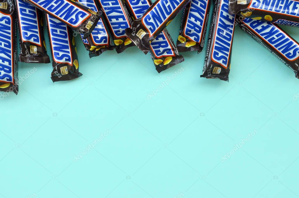 KHARKOV, UKRAINE - OCTOBER 2, 2019: Many Snickers chocolate bars lies on pastel blue paper. Snickers bars are produced by Mars Incorporated. Snickers was created by Franklin Clarence Mars in 1930