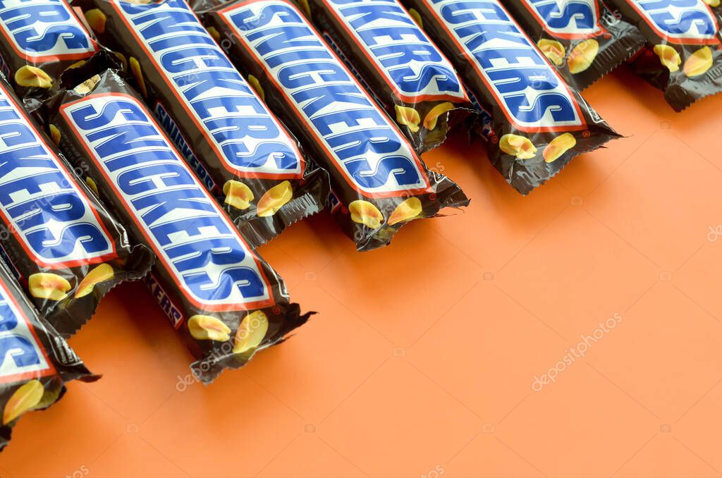 KHARKOV, UKRAINE - OCTOBER 2, 2019: Many Snickers chocolate bars lies on pastel orange paper. Snickers bars are produced by Mars Incorporated. Snickers was created by Franklin Clarence Mars in 1930