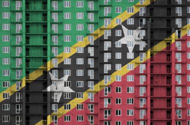 Saint Kitts ve Nevis bayrağı, yapım aşamasında olan çok katlı bir binanın boyalı renkleriyle resmedildi. Büyük tuğla duvar zemininde desenli pankart
