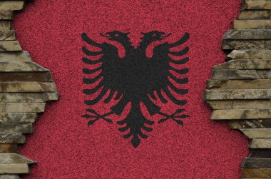 Arnavutluk bayrağı, eski taş duvardaki boya renkleriyle tasvir edilmiş. Kayalık duvar arkaplanındaki desenli pankart