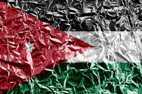 Jordan flag depicted in paint colors on shiny crumpled aluminium foil close up. Textured banner on rough background
