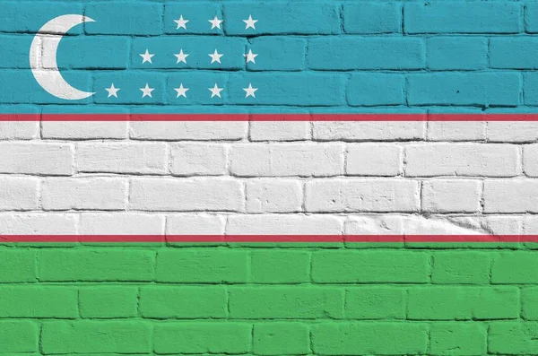 Uzbekistan flag depicted in paint colors on old brick wall close up. Textured banner on big brick wall masonry background