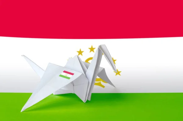 Tajikistan flag depicted on paper origami crane wing. Oriental handmade arts concept