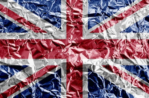 Great britain flag depicted in paint colors on shiny crumpled aluminium foil close up. Textured banner on rough background