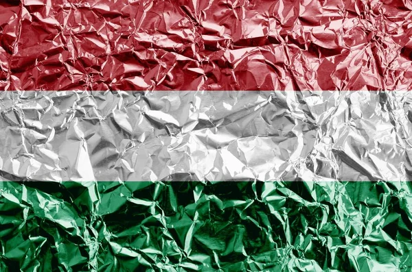 Hungary flag depicted in paint colors on shiny crumpled aluminium foil close up. Textured banner on rough background