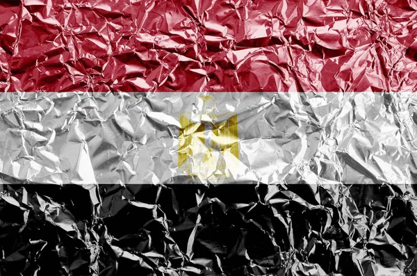 Egypt flag depicted in paint colors on shiny crumpled aluminium foil close up. Textured banner on rough background