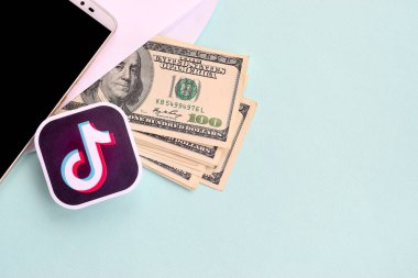 Tiktok kağıt logosu dolar ve akıllı telefon dolu bir zarfla yatar.