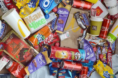 Ünlü yiyecek ve içecek üreticilerinin yenilebilir ürünlerinden bir sürü tek kullanımlık çöp yığını. Soda kutuları ve çikolata ambalajları yığınla.