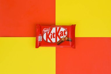 Kırmızı ambalajlı Kit Kat çikolataları sarı ve kırmızı arka planda yatar. Kit Kat, Birleşik Krallık 'ta Rowntree' s of York tarafından yaratıldı ve şimdi küresel olarak Nestle tarafından üretiliyor.
