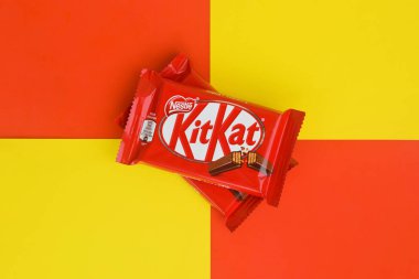 Kırmızı ambalajlı Kit Kat çikolataları sarı ve kırmızı arka planda yatar. Kit Kat, Birleşik Krallık 'ta Rowntree' s of York tarafından yaratıldı ve şimdi küresel olarak Nestle tarafından üretiliyor.