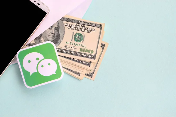 Логотип Wechat бумага лежит с конвертом, полным долларовых купюр и смартфона — стоковое фото