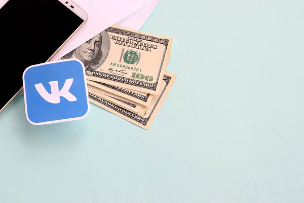 Vkontakte paper logo lies with envelope full of dollar bills and smartphone — Stock Photo, Image