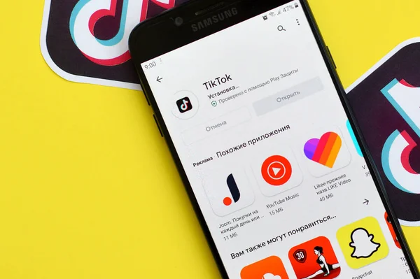 Tiktok application in playmarket on samsung smartphone screen on yellow background. TikTok is a popular video-sharing social networking service owned by ByteDance — Stock Photo, Image