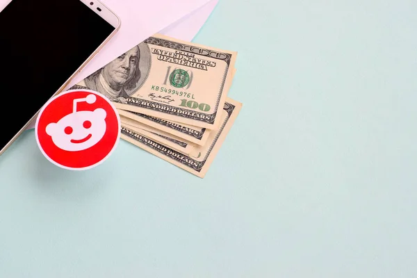 Логотип Reddit бумага лежит с конвертом, полным долларовых купюр и смартфона — стоковое фото